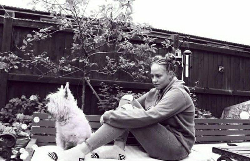 A black and white image of a girl sitting on a garden bench with a dog